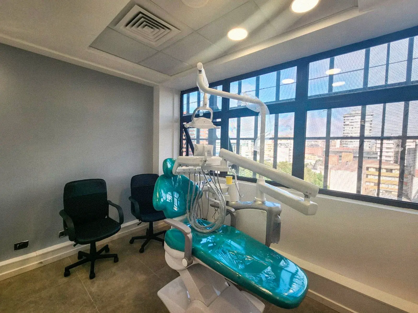 Box de atención dental con sillón turquesa frente a un ventanal